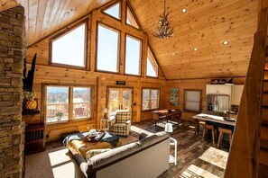 A spacious log cabin interior with a large dining area, a cozy living room with a sofa, and a kitchen with a refrigerator. - Cookie Top Mountain Chalet (Caldwell)