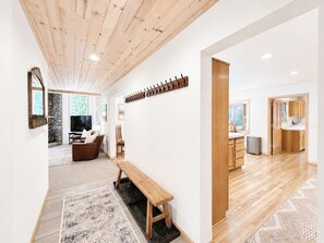 A modern interior with a wooden ceiling, a stone fireplace, a seating area with a bench, and a kitchen visible through an open doorway. - Family Basecamp - Close to Lake Tahoe, Beaches, Trails & Ski Resorts (Tahoe City)