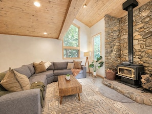 A cozy living room with a stone wall, a fireplace, a sofa, and a coffee table. - Family Basecamp - Close to Lake Tahoe, Beaches, Trails & Ski Resorts (Tahoe City)