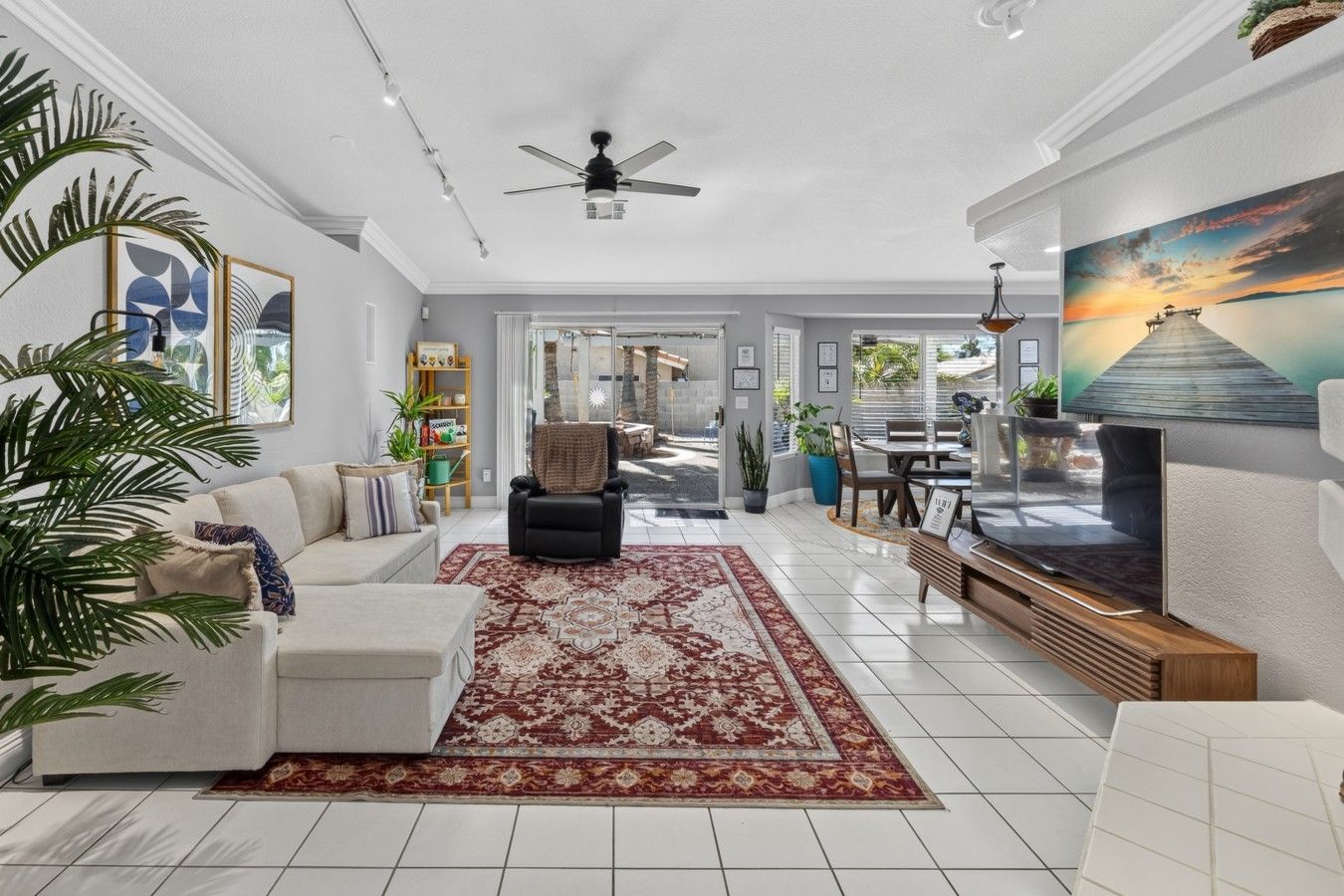 A spacious living room with a large TV, a ceiling fan, and a view of the outdoors.