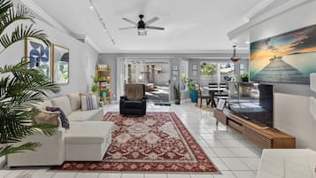 A spacious living room with a large TV, a ceiling fan, and a view of the outdoors.