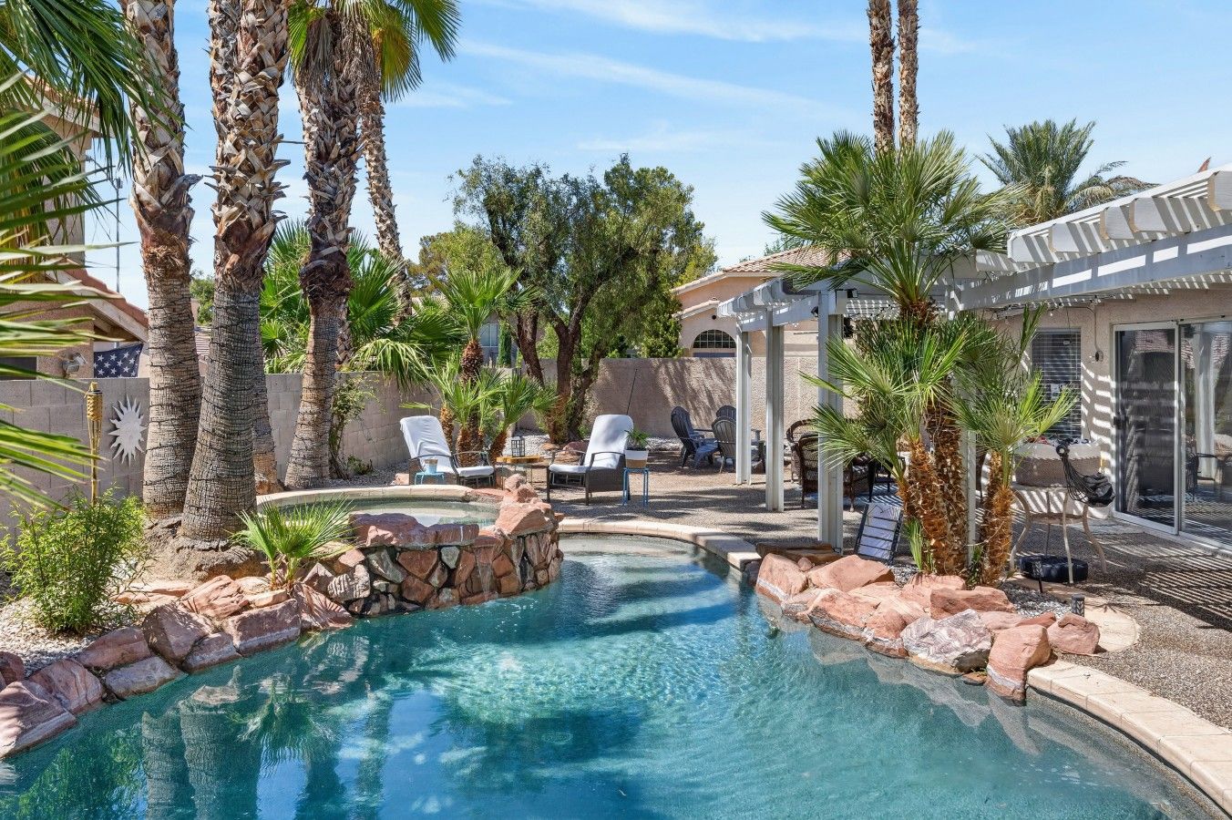 A swimming pool with a stone border, surrounded by palm trees and lounge chairs.