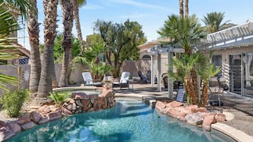 A swimming pool with a stone border, surrounded by palm trees and lounge chairs.