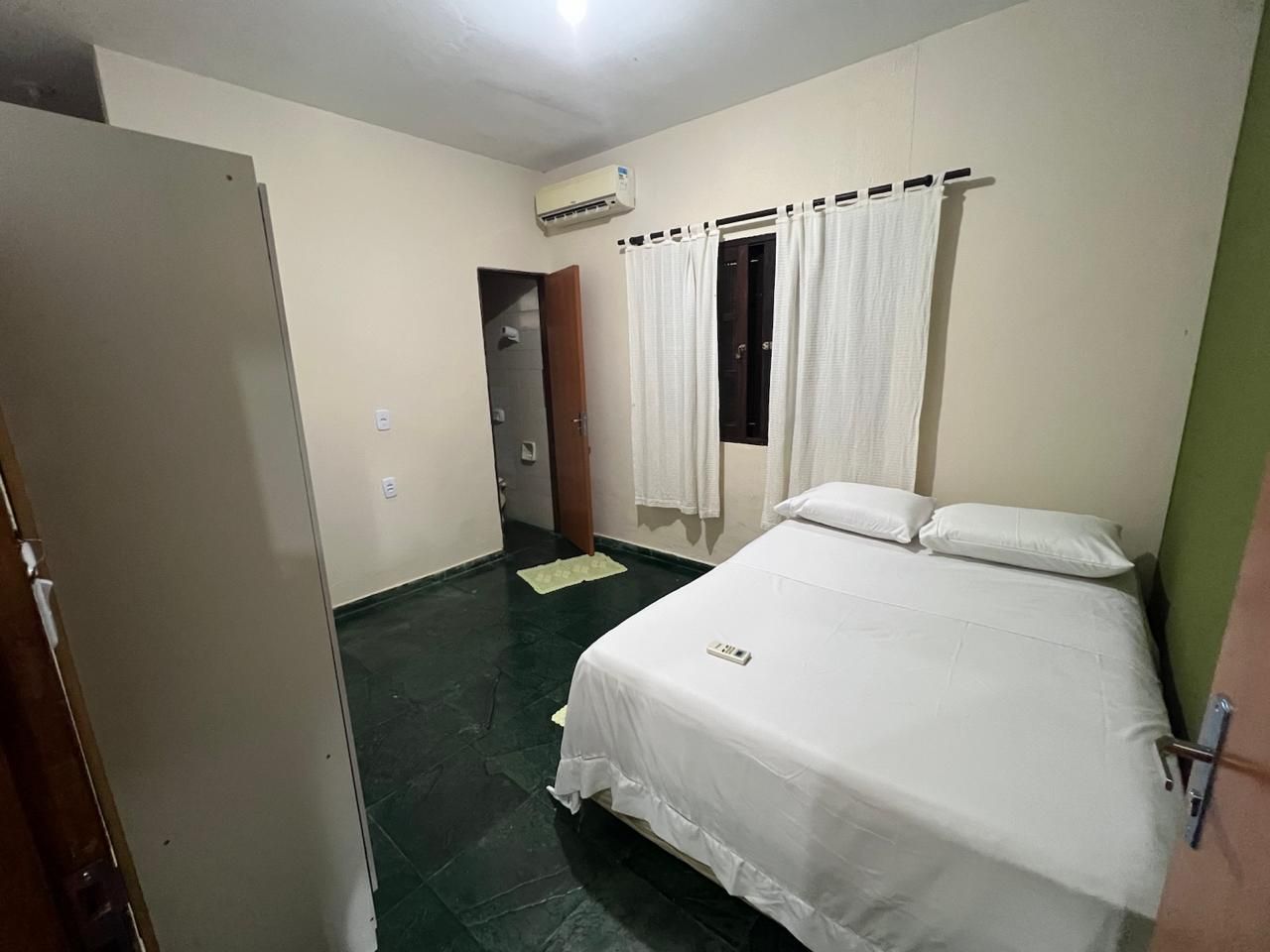 A hotel room with a bed, a door, an air conditioning unit, and a window with curtains.