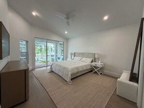 A bedroom with a bed, bedside tables, a TV, and a view through a glass door to an outdoor area. - Waterfront, Private Pool, Close to Beaches, Best of Marco! (Marco Island)