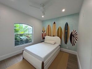 Ein Schlafzimmer mit Bett, Fenster, Deckenventilator und einer Wand mit Surfboard-Kunst.