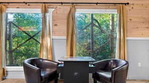 A room with two leather chairs, a small table, and a view of greenery through large windows with curtains. - Sunset Ridge View by Avantstay Hot Tub + Game Room Mountain Views Near Dollywood (Sevierville)