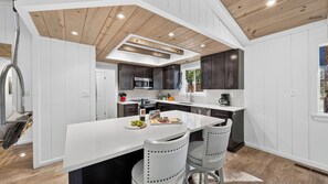 Een moderne keuken met een centraal eiland, donkere kasten en een houten plafond.