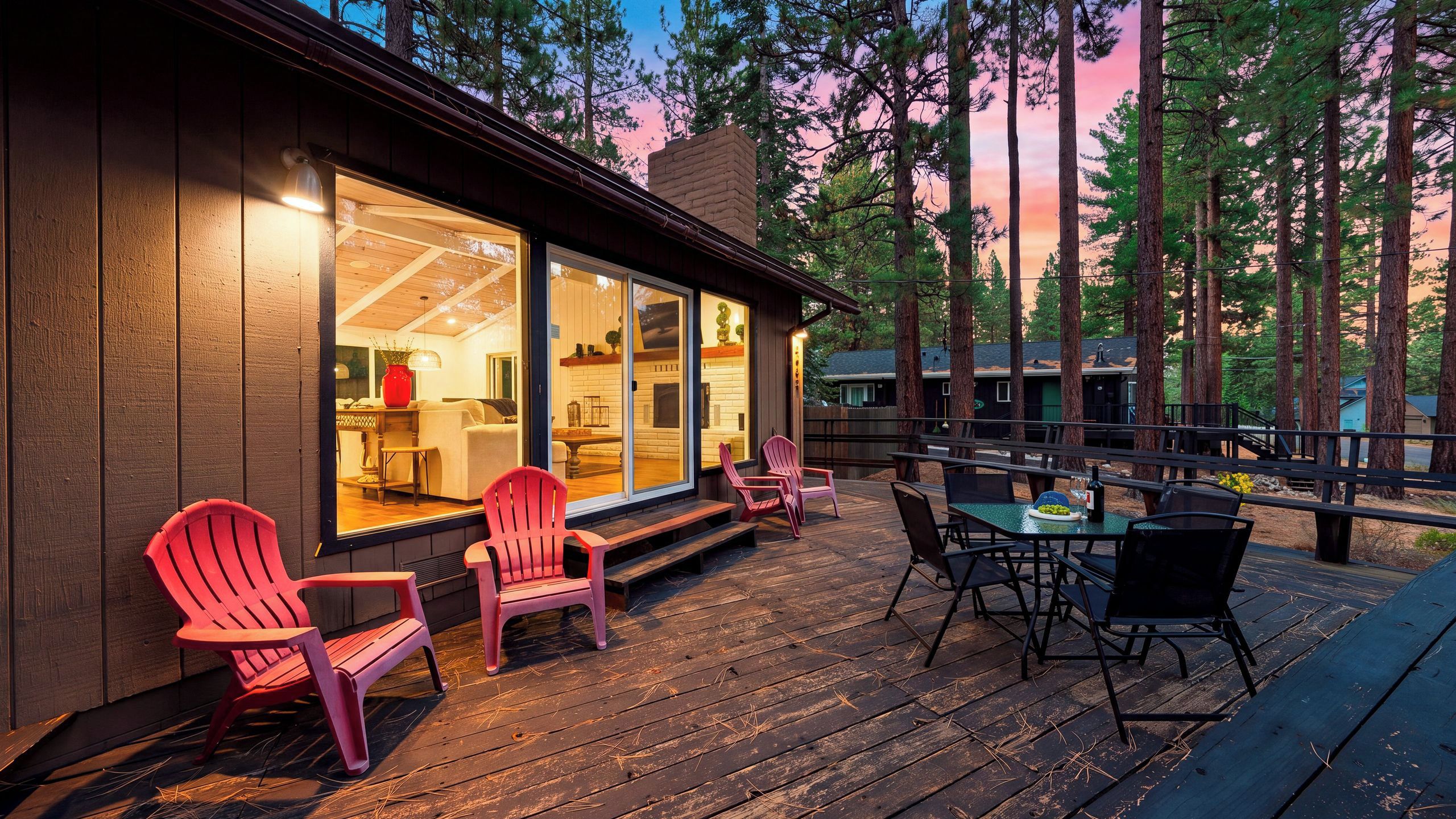 A wooden deck with outdoor seating, a glass door leading to a kitchen area, and a view of tall trees.