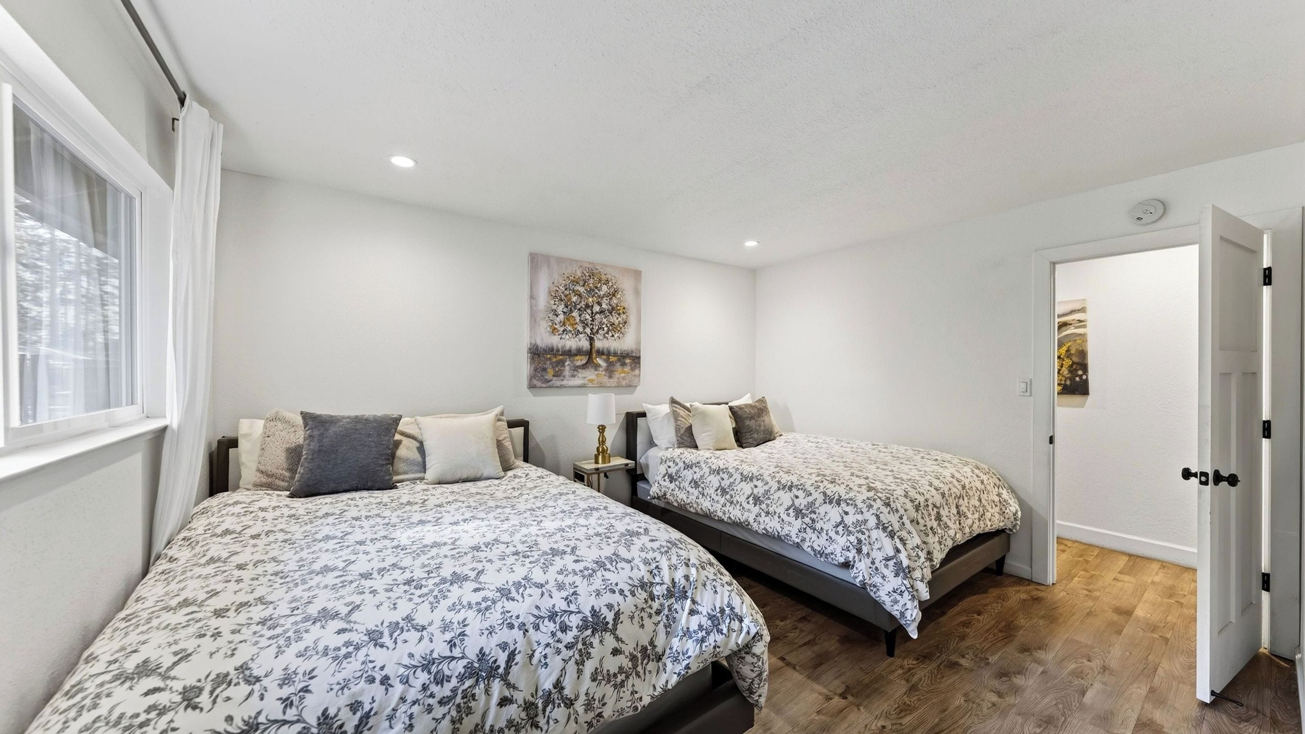A bedroom with two beds, a painting, a nightstand, and a door.