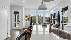 A modern kitchen with a central island, large windows, and a dining area with a view. - High Note by Avantstay 3-story Modern Townhome + Balcony Walk to Coffee + Near Broadway (Nashville)