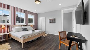 A modern bedroom with a bed, bedside tables, a desk with a chair, a TV, and a window with a view of the outside. - High Note by Avantstay 3-story Modern Townhome + Balcony Walk to Coffee + Near Broadway (Nashville)