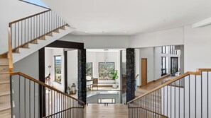 A modern interior with a staircase leading to a balcony, large windows, and a stone pillar. - Castle Black by Avantstay Mountain & City Views Hot Tub + Sauna & Gym Trails to Mt Sanitas (Boulder)