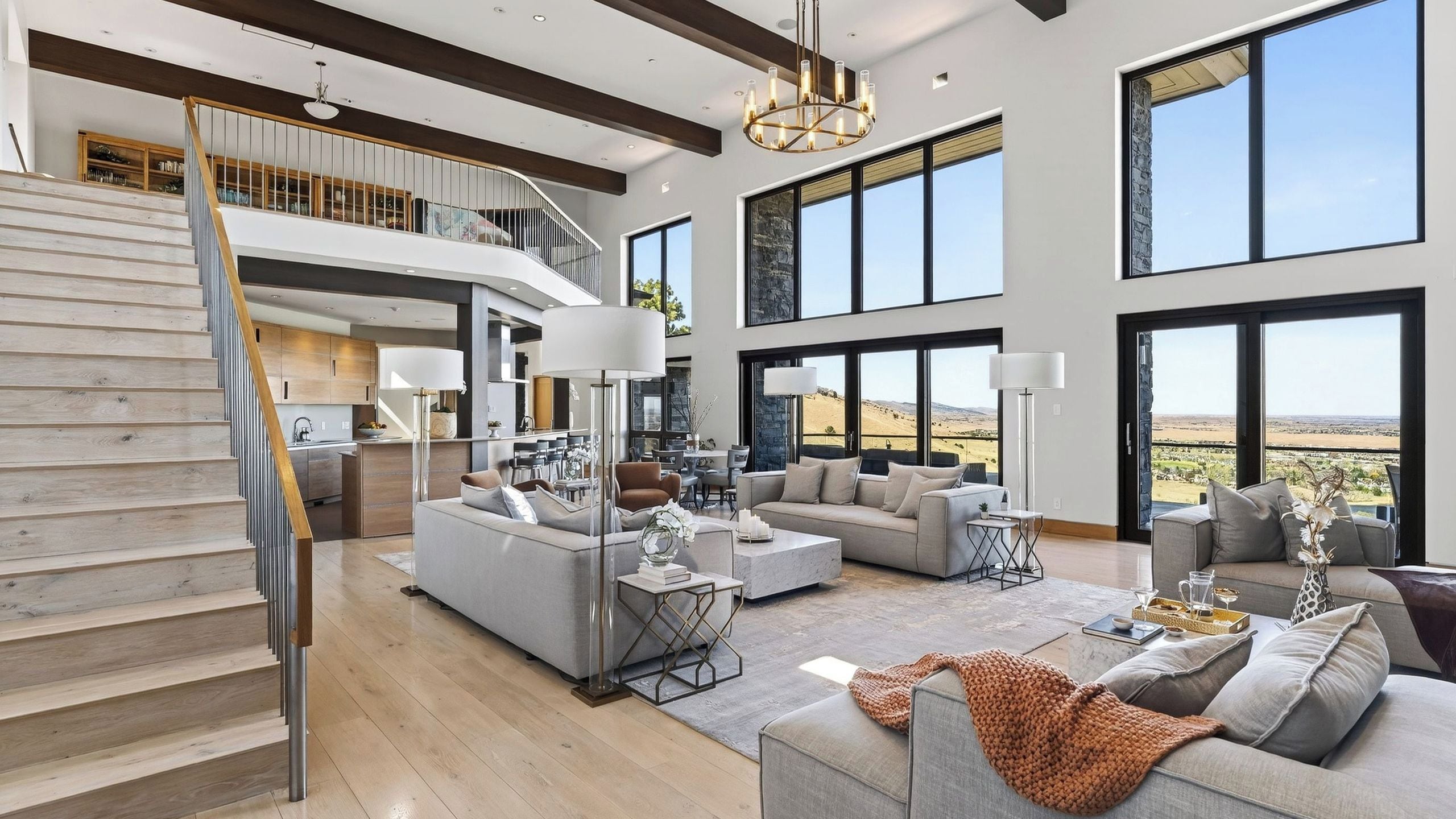 A spacious living area with a staircase, large windows, and a view of the landscape.
