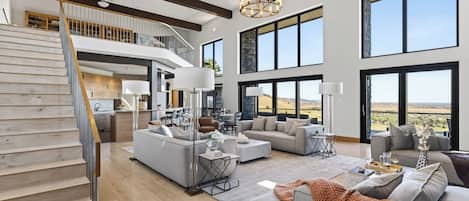 A spacious living area with a staircase, large windows, and a view of the landscape.