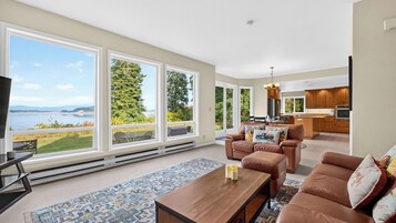 A spacious living room with large windows, a fireplace, and a view of a lake.