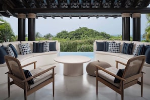 A modern outdoor seating area with a curved sofa and two chairs, a round table, and a view of the ocean. - Villa La Perla: 4BR Four Seasons Villa w/ Private Pool, Chef & Resort Access (Punta Mita)