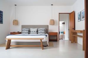 A bedroom with a bed, bedside tables, a nightstand, a wooden bench, and a hanging light fixture. - Villa La Perla: 4BR Four Seasons Villa w/ Private Pool, Chef & Resort Access (Punta Mita)