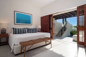 Un dormitorio con cama, mesita de noche, lámpara, un cuadro enmarcado, un banco y vistas a un área exterior con una escalera.