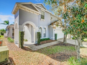 A two-story house with a garage, a driveway, and a well-maintained lawn. - Elegant 5BR Home w/ Pool Spa Near Disney (Davenport)