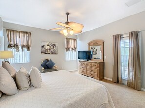A bedroom with a bed, a television, a dresser, a ceiling fan, and curtains. - Elegant 5BR Home w/ Pool Spa Near Disney (Davenport)