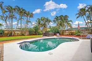 A swimming pool with a wooden deck, surrounded by palm trees and a wooden fence. - Heated Pool, Luxury Furnishings, Equipped Kitchen, Close to Beach and Downtown (Stuart)