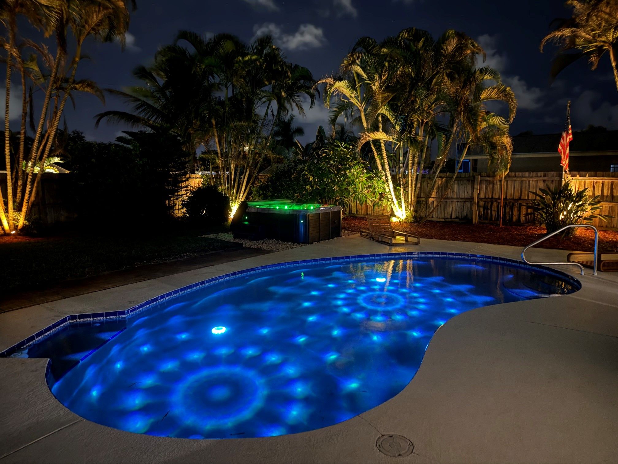 Una piscina con un diseño de iluminación azul único, rodeada de palmeras y una valla de madera.