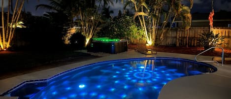 A swimming pool with a unique blue light design, surrounded by palm trees and a wooden fence.