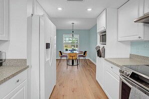 A kitchen with white cabinets, a granite countertop, a dining table with chairs, a microwave, and a stove. - Heated Pool, Luxury Furnishings, Equipped Kitchen, Close to Beach and Downtown (Stuart)