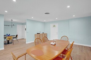 A dining area with a wooden table and chairs, a kitchen in the background, and a door with a sign. - Heated Pool, Luxury Furnishings, Equipped Kitchen, Close to Beach and Downtown (Stuart)