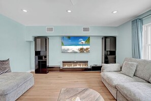 A living room with a fireplace, a sofa, and a painting of a beach scene. - Heated Pool, Luxury Furnishings, Equipped Kitchen, Close to Beach and Downtown (Stuart)