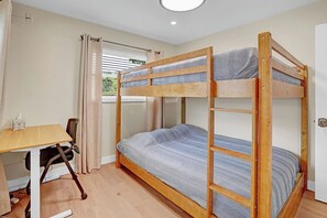 A bunk bed room with a desk and chair, a window with curtains, and a door. - Heated Pool, Luxury Furnishings, Equipped Kitchen, Close to Beach and Downtown (Stuart)