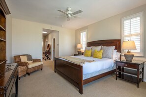 Quarto com cama grande, mesa de cabeceira com abajur, uma cadeira e ventilador de teto.