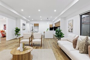 Ein modernes Wohnzimmer mit einer Couch, Sesseln, einem Couchtisch und einer Küche im Hintergrund.