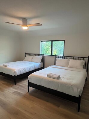 A room with two single beds, a ceiling fan, and a window with a view of greenery. - Event Space with secluded pool and yard near Hobby Airport (Houston)