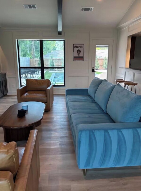 A living room with a blue sofa, a brown leather chair, and a wooden coffee table. - Event Space with secluded pool and yard near Hobby Airport (Houston)
