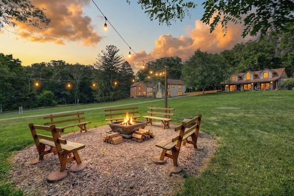 A backyard with a fire pit, picnic tables, and string lights.