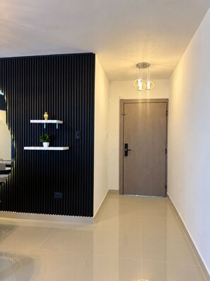 Un couloir moderne avec un panneau vertical foncé, une porte en bois et un luminaire suspendu.