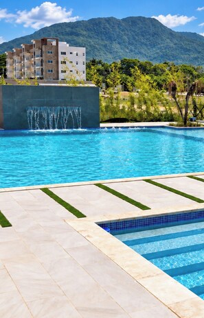 A swimming pool with a waterfall feature, surrounded by a tiled deck and lush greenery. - Puerto Plata 3 BR Near Playa Dorada  2 Pools, A/C, Wi-Fi & Laundry for Families (Puerto plata)
