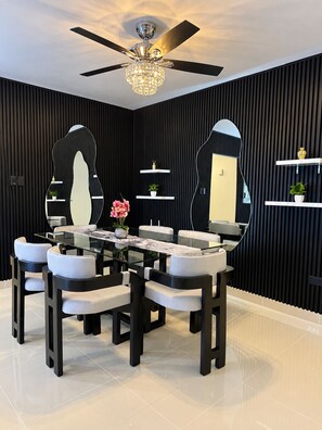 A modern dining area with a glass-top table, black and white chairs, a ceiling fan, and decorative mirrors. - Puerto Plata 3 BR Near Playa Dorada  2 Pools, A/C, Wi-Fi & Laundry for Families (Puerto plata)