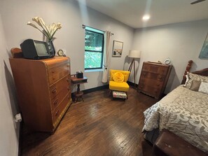 A bedroom with a wooden dresser, a yellow armchair, a bed with patterned bedding, and a window with curtains. - Willa's Retreat in the McCoy Place Lofts (Cave City)
