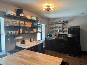 A kitchen with a wooden countertop, a sink, a black refrigerator, and shelves with dishes and kitchenware. - Willa's Retreat in the McCoy Place Lofts (Cave City)