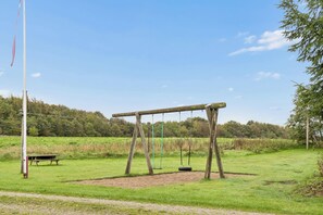 A swing set in a grassy field with a bench and a flagpole in the background. - Peace and cosiness near the Limfjord (Farsø)