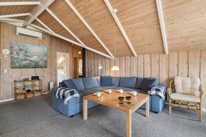 Ein gemütliches Wohnzimmer mit Holzboden, einem blauen Sofa, einem Couchtisch aus Holz und einem Korbstuhl.