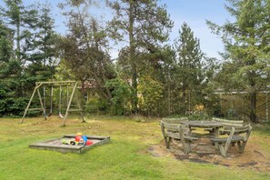 A wooden swing set, a picnic table, and a play area with toys and a sandbox. - Cosy holiday home near Ebeltoft and the beach (Ebeltoft)