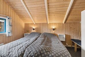 Ein Zimmer mit Holzwänden und -decke, einem Bett mit gemusterten Betttextilien, Nachttischen und einem Fenster mit Vorhängen.