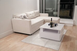 A modern living room with a white sofa, a white coffee table, and a glass door leading to an outdoor area. - 3BR Rotherhithe Home | Gated Parking & Balcony (London)