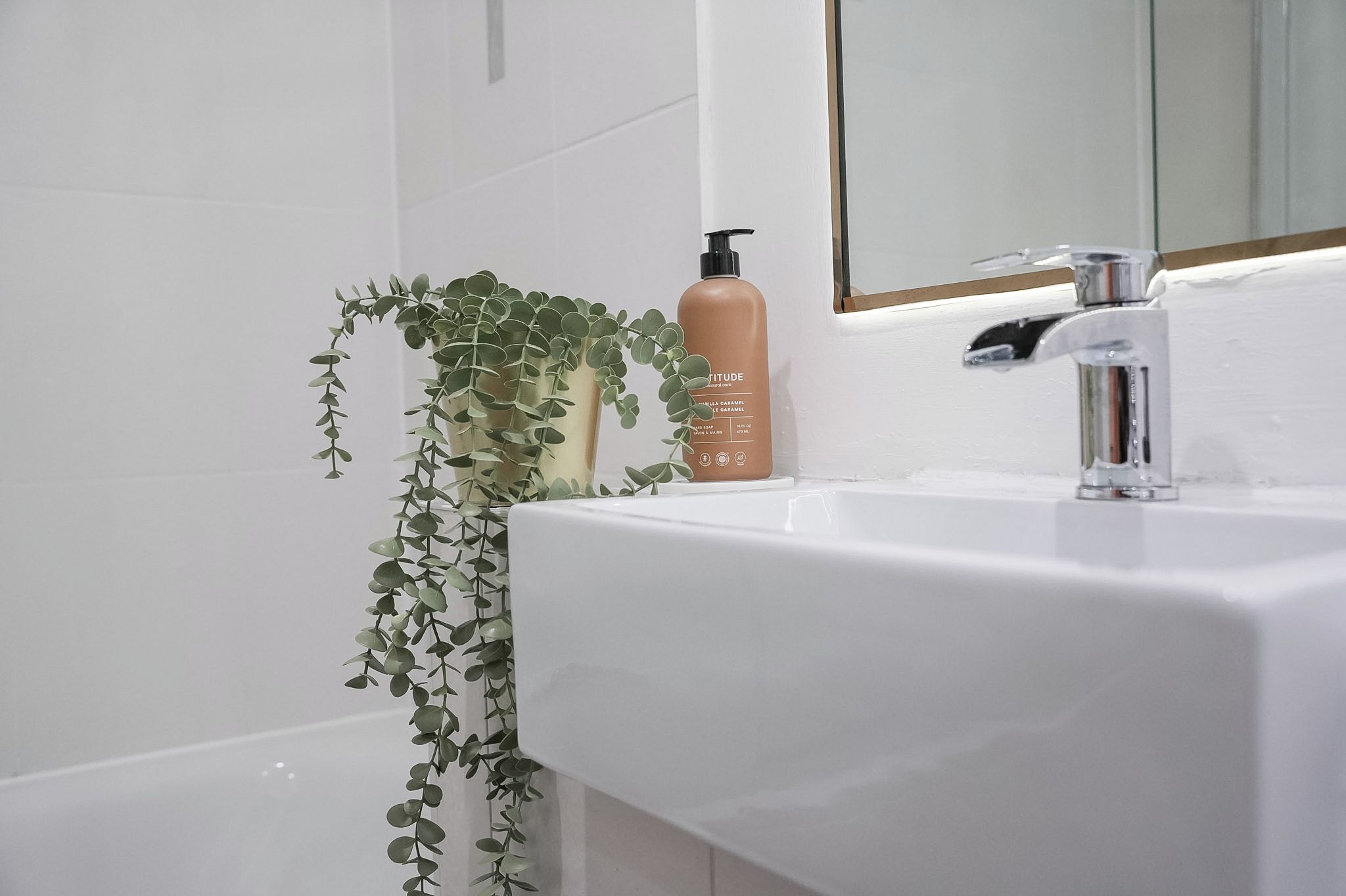 A bathroom with a white sink, a mirror, and a bottle of body lotion.