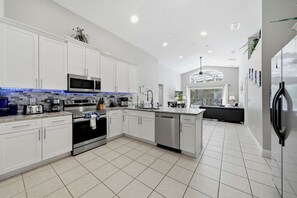 A modern kitchen with white cabinets, stainless steel appliances, and a tiled floor. - Private Pool & Game Room Near Disney Parks (Kissimmee)