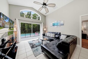 A spacious living room with a black leather sofa, a glass coffee table, and a large window overlooking a swimming pool. - Private Pool & Game Room Near Disney Parks (Kissimmee)